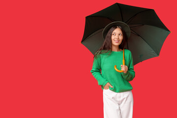 Beautiful young Asian woman with umbrella on red background