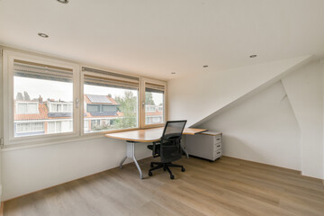 A minimalist office space featuring a desk and chair beside large windows that provide a view of the cityscape outside.