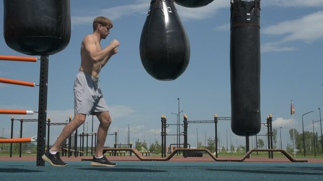 Professional fighter practicing boxing, hitting punching bag on sports ground outside
