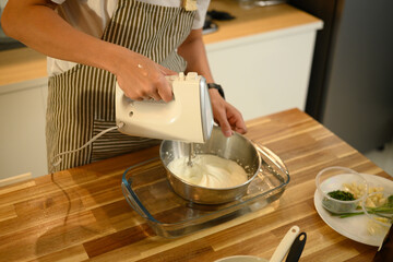 Close up of man using handheld electric mixer to whip cream in a stainless steel bowl