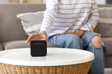 Fototapeta premium Beautiful young woman with wireless portable speaker on table at home, closeup