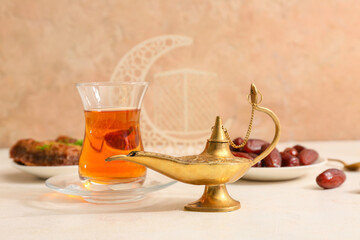 Aladdin lamp and glass cup of tea on white table against beige background. Ramadan celebration
