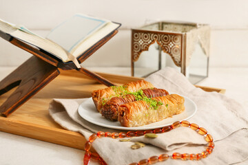 Baklava, Koran and prayer beads on white table against wooden background. Ramadan celebration