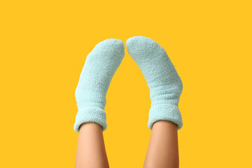 Legs of young woman in warm blue socks on yellow background