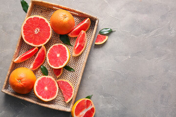 Wicker tray with fresh ripe grapefruits and leaves on grey background