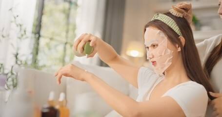 Two Asian women friends applying sheet masks together during beauty daily routine at home. Girl talk, skincare bonding moment, Gen Z lifestyle, self care and relaxing feminine friendship vibe.