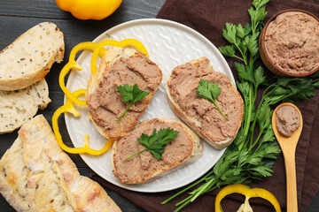 Plate with toasts, bowl of tasty pate, parsley and bell pepper slices on dark wooden background