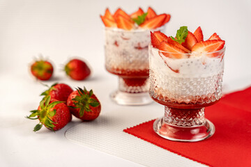 Horizontal photo of desserts with chia seeds and strawberries with mint leaves in a beautiful glass on a red and white background with space for text. Concept of vegan desserts, food blogs