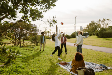 A group of four adult friends aged 25, tossing a volleyball around and having fun as they stand on...