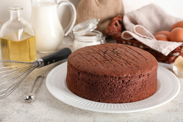 Delicious chocolate sponge cake with ingredients and whisk on light grunge background