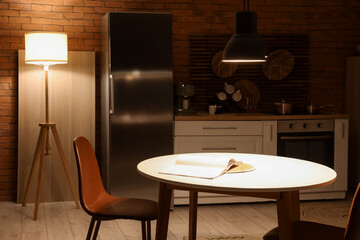 Interior of dark kitchen with counters, dining table and glowing lamps at night