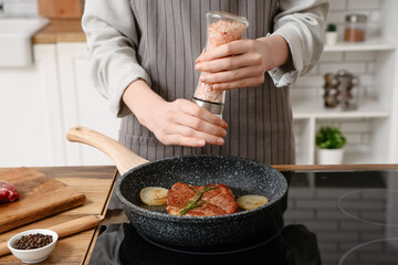 Woman frying tasty steak in kitchen