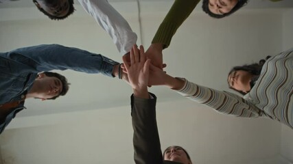 Under view shot of young female teacher with diverse teenagers standing in circle, stacking hands and lifting up in air creating feeling of unity, support and cooperation