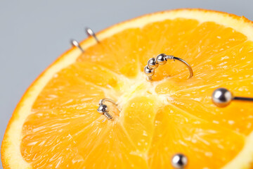 Half of orange fruit with piercing on grey background, closeup