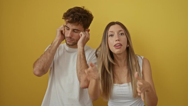 Couple in disagreement, woman arguing while man covers ears against yellow background, capturing emotions and tension in their relationship.