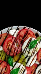 Colorful Caprese salad beautifully arranged with ripe tomatoes, fresh mozzarella, and basil drizzled with balsamic glaze served on a white plate