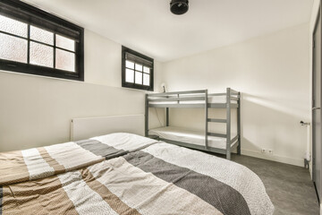 A modern minimalist bedroom featuring a twin bunk bed and stylish gray decor with natural light filtering through large windows.