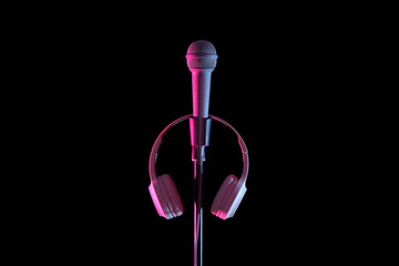 Stand with professional microphone and headphones near black wall in recording studio