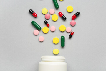White bottle with scattered pills on grey background, closeup
