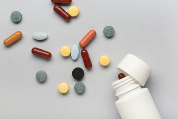 Bottle with different scattered pills on grey background, closeup