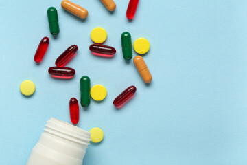 Bottle with different scattered pills on blue background, closeup