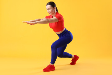 Woman in sportswear exercising on orange background