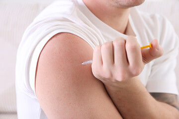 Man making insulin injection into his arm indoors, closeup. Diabetes
