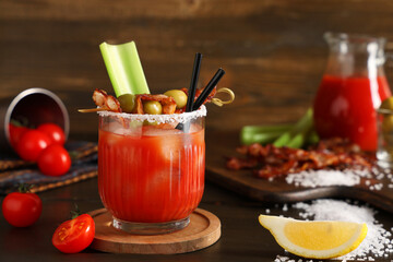 Glass of bloody mary cocktail with bacon, olives and celery on wooden background