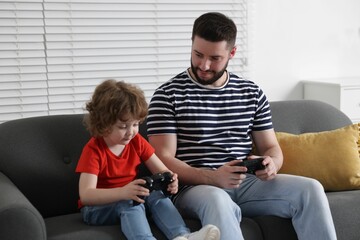 Happy father and his son playing with game controllers together on sofa at home