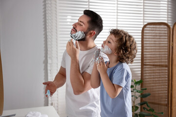 Happy father and his son with shaving cream on their faces in bathroom