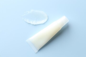 Moisturizing lip balm and tube on light blue background, top view