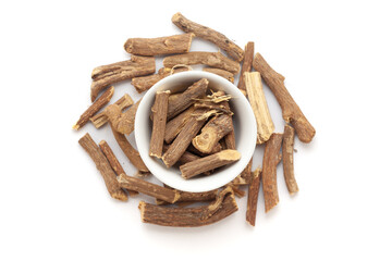 A bowl of Organic Liquorice or Mulethi (Glycyrrhiza glabra), placed over a heap of liquorice roots. Isolated on a white background.