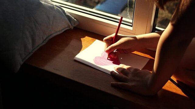 Preteen daughter carefully crafting mother's day, 8 march or birthday card for mom sitting by window at home. Concept of family love, tradition and celebration
