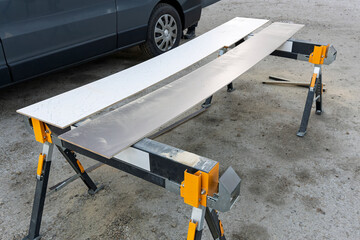 Brown and White Laminate Wood Board Supported on Saw Horse Woodwork Trestle at Outdoor Construction...