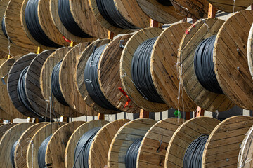 Tghtly packed wooden reels filled with heavy duty black cable at outdoor industrial depot.