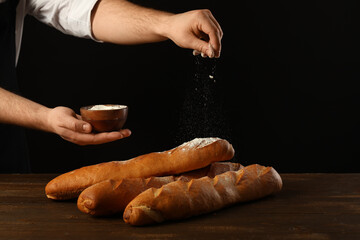 Man sprinkling flour on fresh baguettes against black background