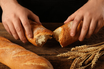 Man with fresh baguettes and wheat on wooden table