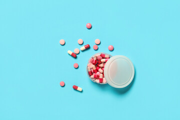 Jar with different pink pills on blue background