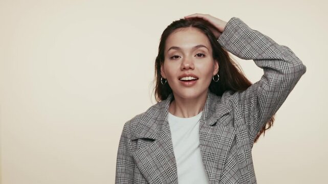 A young woman in a casual outfit flips her hair with a smile, expressing confidence and vitality in a studio setting.