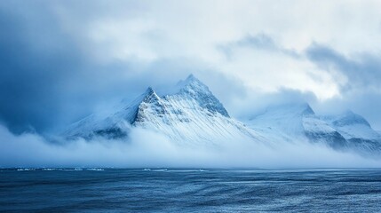 Fototapeta premium Majestic snow-covered mountains shrouded in mist near the cold ocean, a serene landscape