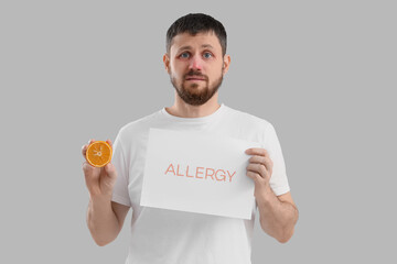 Young man holding paper with word ALLERGY and orange on light background