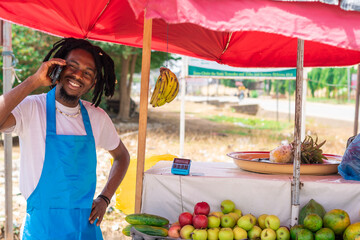 African american trader in a market space making use of mobile phone. excited businessman on dreads...