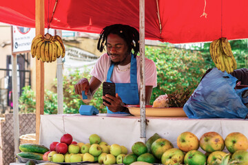 African fruit seller businessman showcasing the modern NFC payment method, with hands holding a POS...