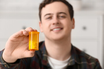 Fototapeta premium Happy young man with bottle of pills at home, closeup