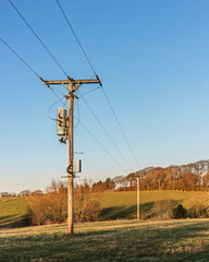 Wooden Electricity Utility Pole with Overhead Power Lines and Transformers in a Field Against a...