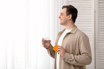 Fototapeta premium Young man with blister pack of pills and glass of water at home