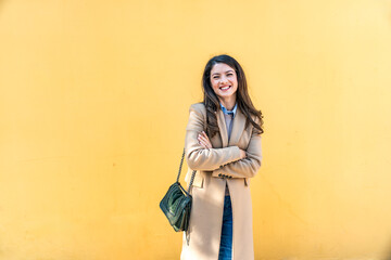 Fototapeta premium Portrait of successful businesswoman, office worker in corporate business, standing against yellow or orange wall in formalwear. Strong independent professional occupation female leader posing.