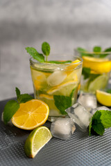 Lemonade drink with mint and lemon on a dark textured surface with scattered ice and citrus fruits. Soft focus. Food photography of citrus lemonade with space for text. Vertical photo