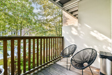 A serene balcony scene featuring two stylish chairs amidst lush green trees, providing a peaceful...