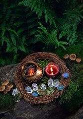 witch cauldron, burning candle and crystals in forest, dark natural background. occult ceremony,...